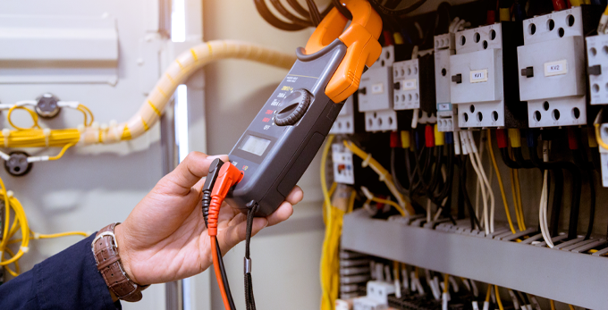 A electrician taking measurements of multimeter electrical current in control panel.