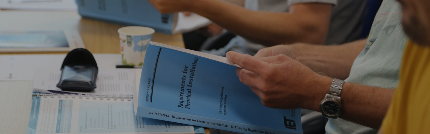 Electricians on a training course, reading the 2018 British standard requirements for electrical installations booklet.