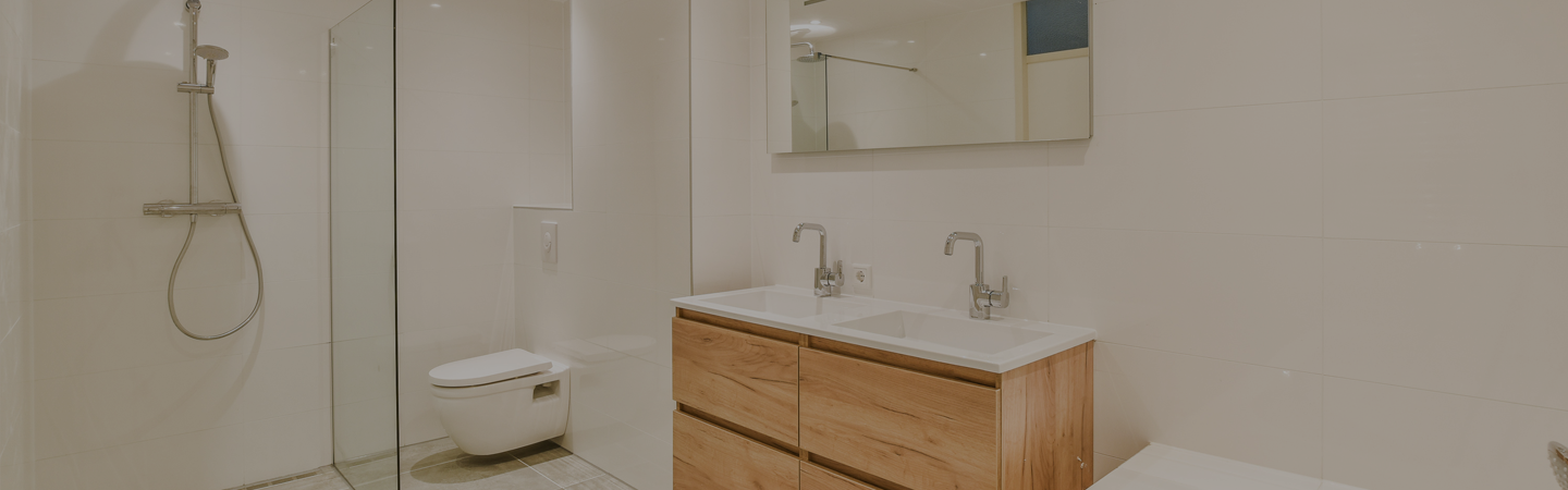 White modern bathroom, with a dual sink, toilet, walk in shower and LED ceiling lighting.