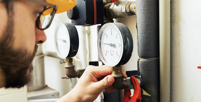 A plumber installing and reviewing a dialled gas pressure meter for household heating system