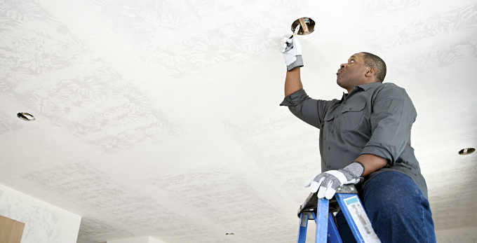 An electrician working on a second fix of ceiling light wiring in a household, whilst safely standing on a step ladder.