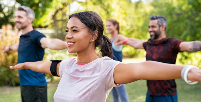 A group of multiethnic people, smiling and stretching arms during a yoga class outdoors on a sunny day.
