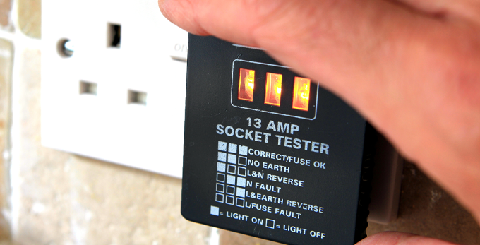 An electrician using a UK 13 AMP socket tester to show socket condition and safety score.