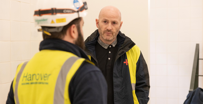 An NICEIC approved contractor, discussing a job in hand with another contractor. Wearing branded NICEIC work wear.