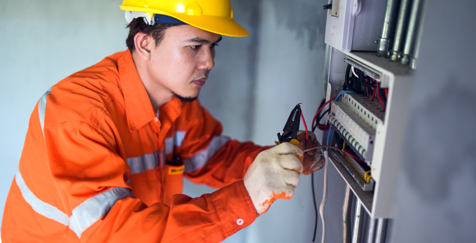 An electrician where safety gear, repairing an electric board, in an office corridor.