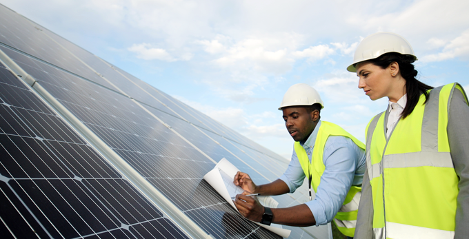 Two team members reviewing the installation of solar panels, cross referencing printed plans and making notes.