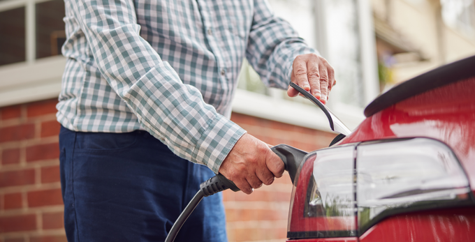 A male in a checked shirt, plugging in the charging unit into red electric car at home