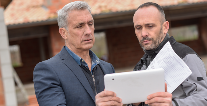 A client and a contractor talking and looking at a digital tablet outside.