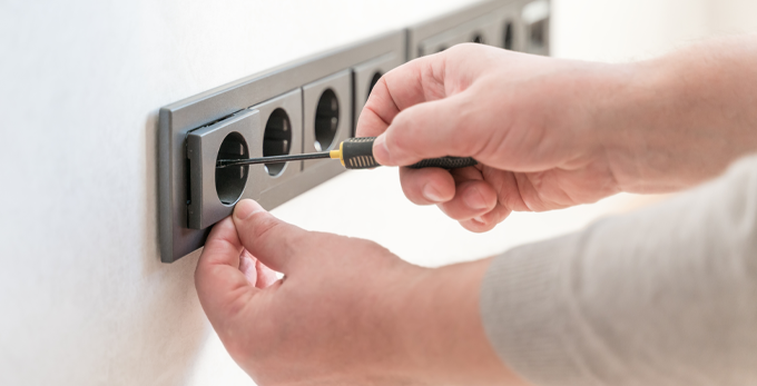Close-up male hands install a socket with a screwdriver. Finishing work in a new apartment. The man is installing electrical wiring. Home repair and installation of electrical outlets on the wall using a professional tool.