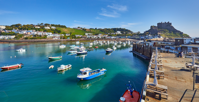 Gorey Harbour in the Jersey, Channel Islands, United Kingdom. with fishing and pleasure boats, the pier bullworks and Gorey Castle in the background with a blue sky.