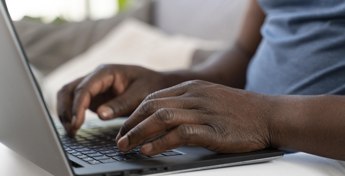 A man working from home on a laptop, a close up of the mans hands typing on a keyboard.