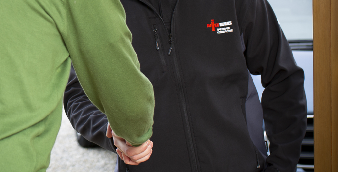 An NICEIC approved contractor, wearing a branded jacket is shaking hands with a customer outside of the households front door.