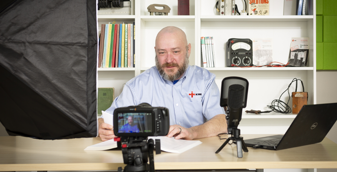 An NICEIC employee hosting the internal low carbon fix podcast, being recorded whilst sat at a deck with a professional constructed set.