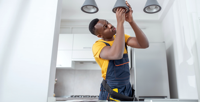 A tradesman installing the final third fix of ceiling lights, in a contemporary kitchen.