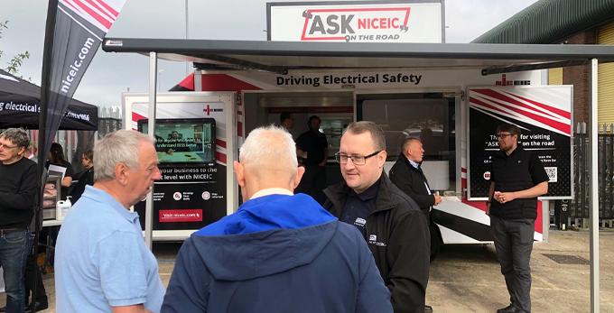 ASK NICEIC 2023 tour, male contractors standing in front of an NICEIC branded vehicle, on a sunny day, coming together to at wholesaler REXEL venue in Norfolk, June 2023.