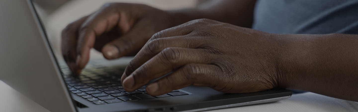A man working from home on a laptop, a close up of the mans hands typing on a keyboard.