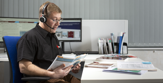 A dedicated account manager sat at a work deck, talking on the phone whilst looking through the NICEIC Inspection, Testing and Certification guide.
