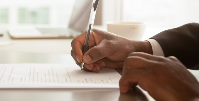 business man sitting at an office deck, holding a pen to sign contract papers.