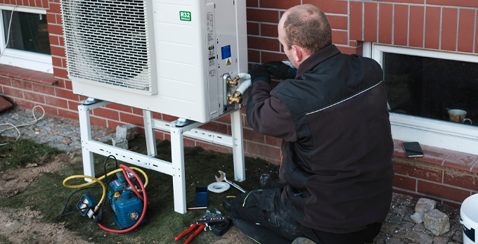 A man installing a heat pump system outdoors for a single family household