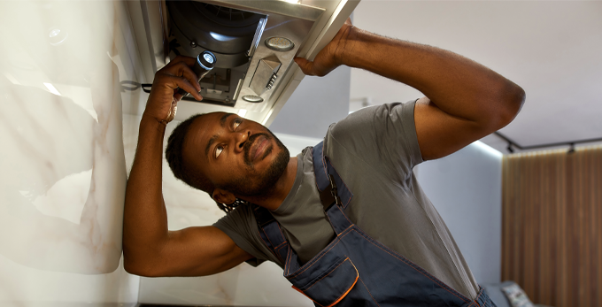 A contractor using a torch to inspect  oven ventilation hood in a kitchen.